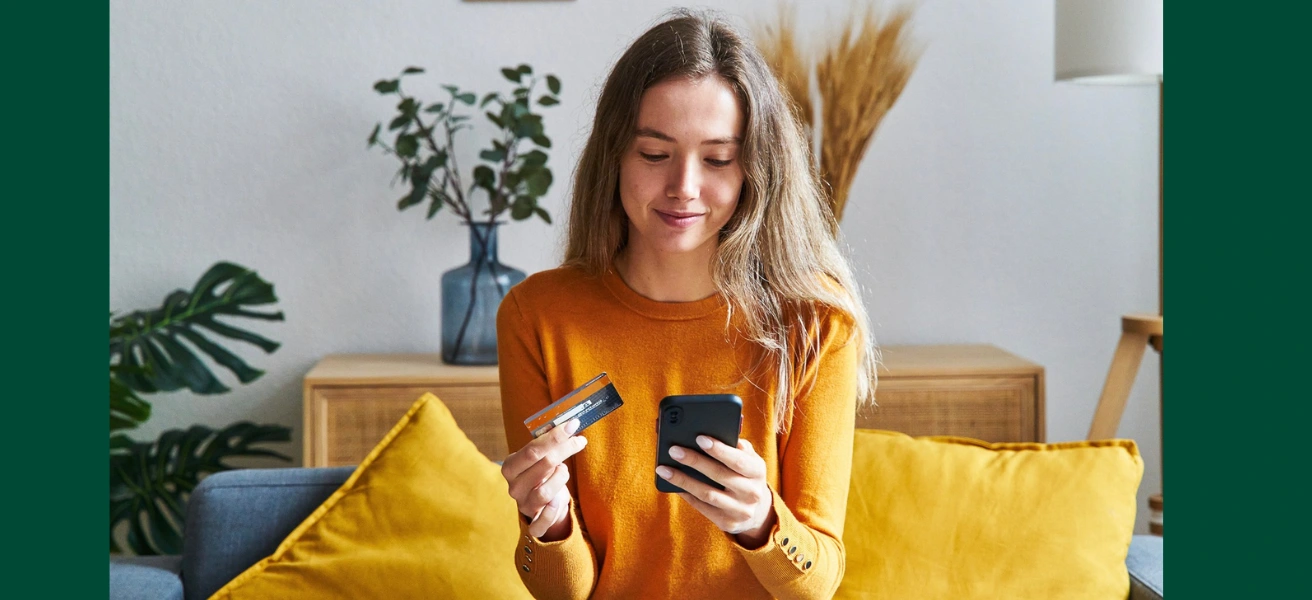 Woman smiling while holding a credit card in one hand, and her phone in the other.