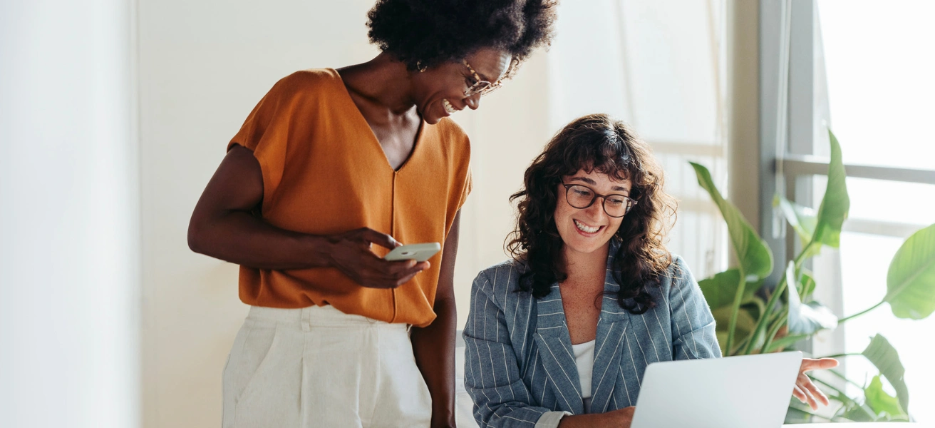 Two women smiling while working together on a laptop, representing teamwork and affiliate collaboration.